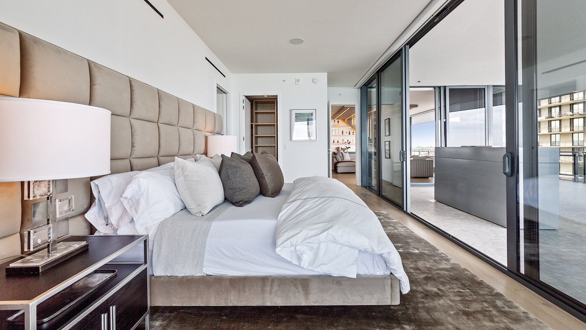 Eighty Seven Park, Miami Beach luxury and ultra luxury condos bedroom with a padded headboard, sliding glass partition, adjoining terrace, and sightline into the living area.