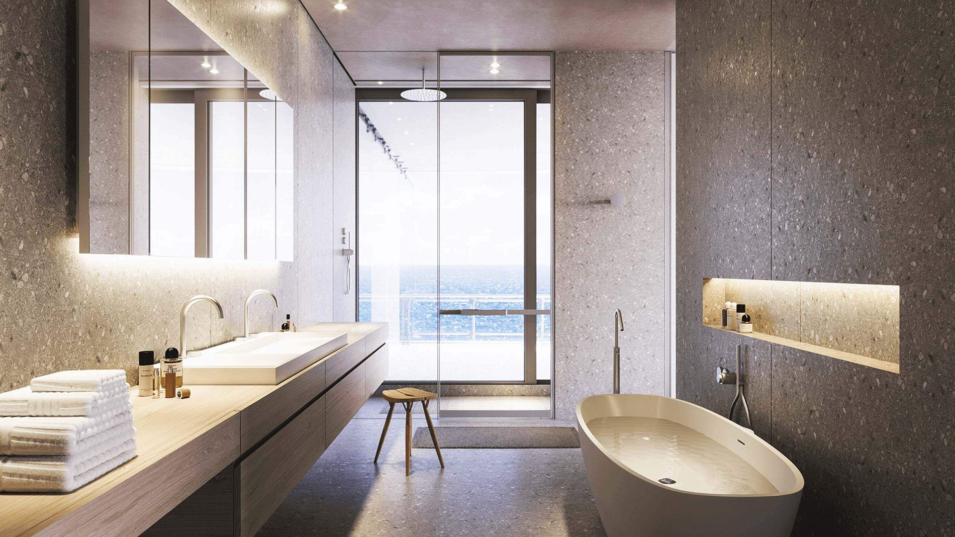 Eighty Seven Park, Miami Beach luxury and ultra luxury condos spa bathroom with a freestanding tub, floating double vanity, glass shower, and ocean view beyond.