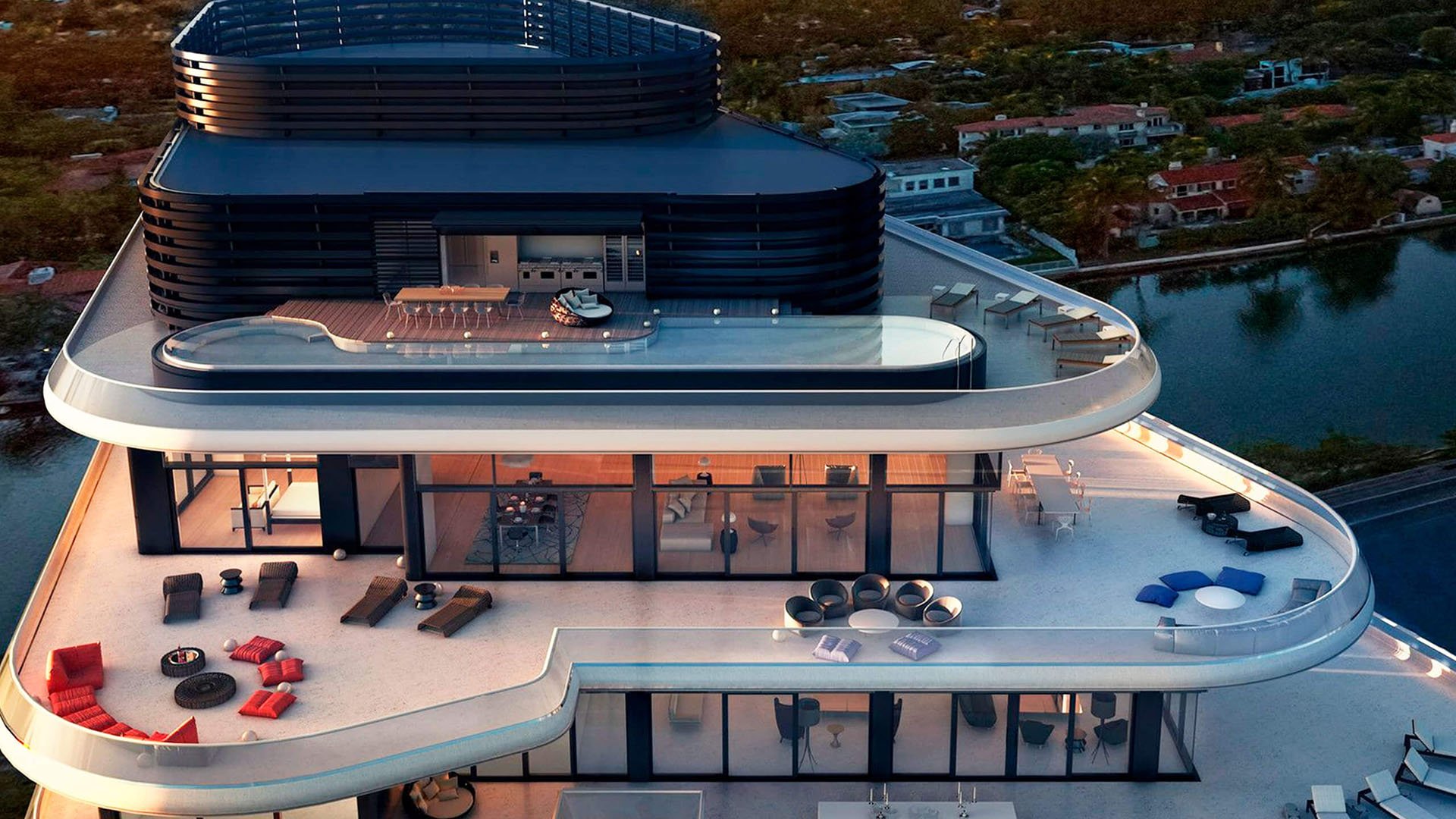 Aerial rooftop terrace view of Faena House in Miami Beach, luxury and ultra luxury condos with a long rooftop pool, outdoor lounge areas, glass walls, and a waterway backdrop at dusk.