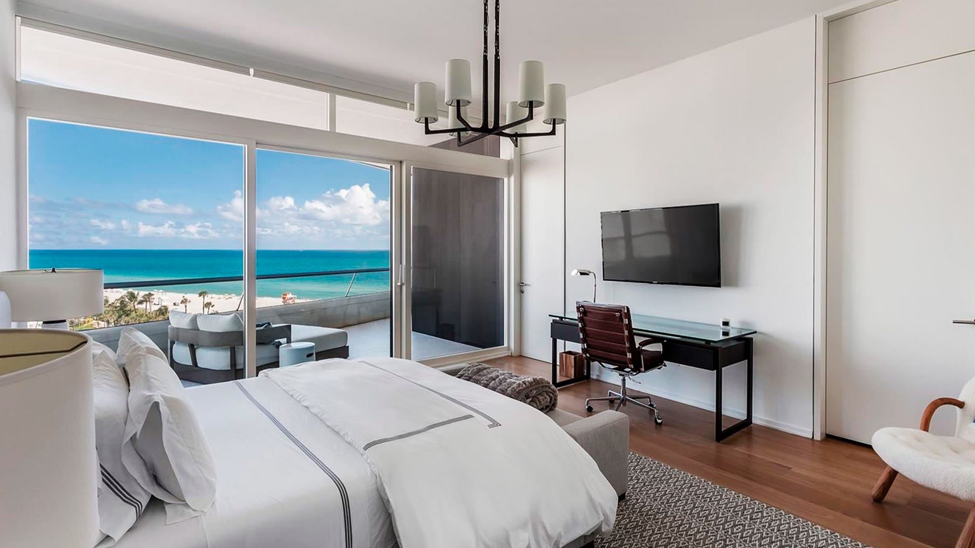 Bedroom with terrace seating and ocean view at Faena House in Miami Beach, luxury and ultra luxury condos featuring wood floors, a desk, and wide sliding glass doors to the beachfront balcony.