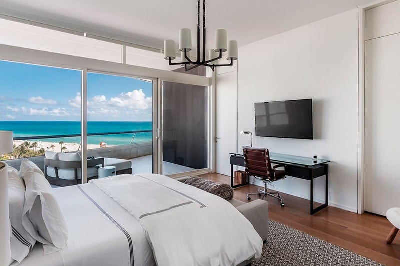 Bedroom with terrace seating and ocean view at Faena House in Miami Beach, luxury and ultra luxury condos featuring wood floors, a desk, and wide sliding glass doors to the beachfront balcony.