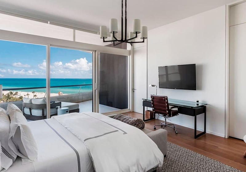Bedroom with terrace seating and ocean view at Faena House in Miami Beach, luxury and ultra luxury condos featuring wood floors, a desk, and wide sliding glass doors to the beachfront balcony.