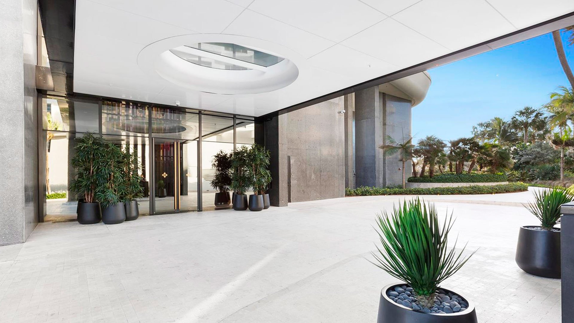 Covered lobby entrance at Faena House in Miami Beach, luxury and ultra luxury condos with a porte cochere, glass doors, circular ceiling skylight, large planters, and tropical landscaping.