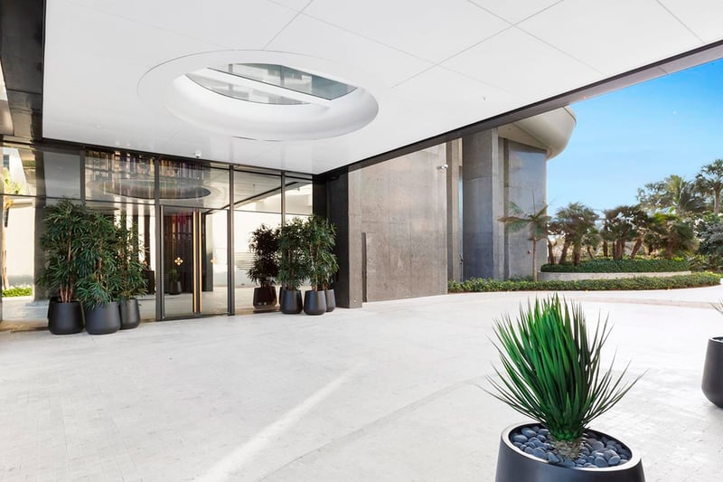 Covered lobby entrance at Faena House in Miami Beach, luxury and ultra luxury condos with a porte cochere, glass doors, circular ceiling skylight, large planters, and tropical landscaping.