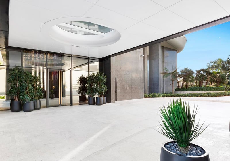 Covered lobby entrance at Faena House in Miami Beach, luxury and ultra luxury condos with a porte cochere, glass doors, circular ceiling skylight, large planters, and tropical landscaping.
