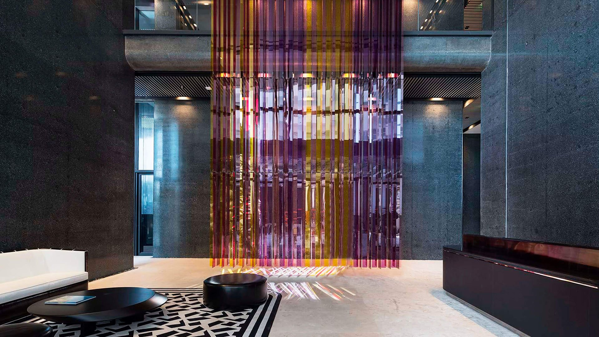 Lobby interior at Faena House in Miami Beach, luxury and ultra luxury condos with dark stone walls, a colorful hanging art installation, lounge seating, and polished floors.