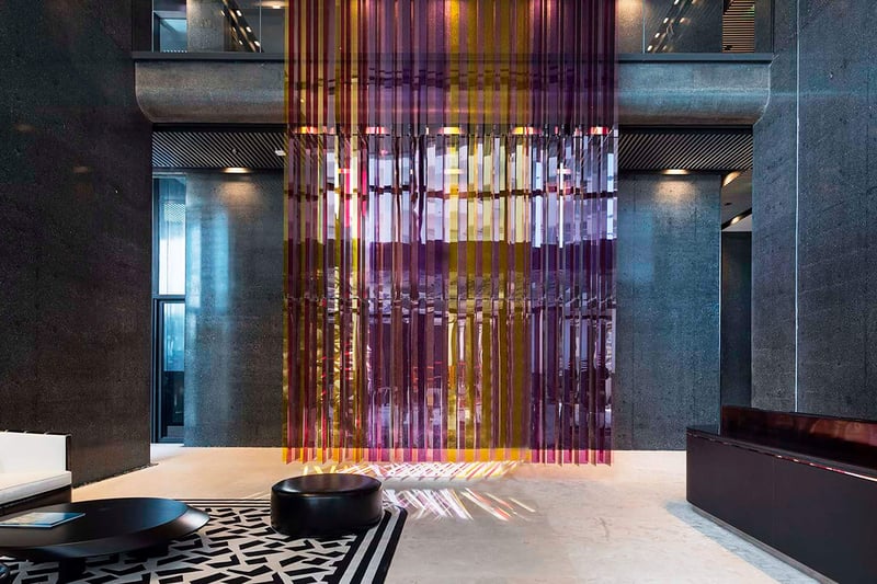 Lobby interior at Faena House in Miami Beach, luxury and ultra luxury condos with dark stone walls, a colorful hanging art installation, lounge seating, and polished floors.
