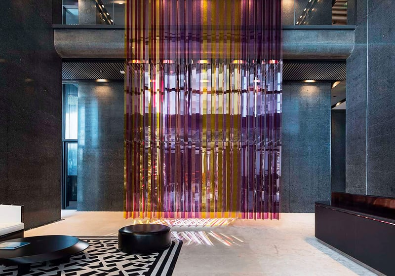 Lobby interior at Faena House in Miami Beach, luxury and ultra luxury condos with dark stone walls, a colorful hanging art installation, lounge seating, and polished floors.