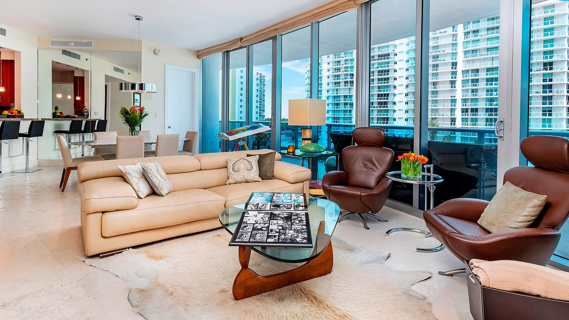 Open-plan living room at Faena House in Miami Beach, luxury and ultra luxury condos with a dining area, breakfast bar, floor-to-ceiling windows, leather lounge chairs, and neighboring tower views.