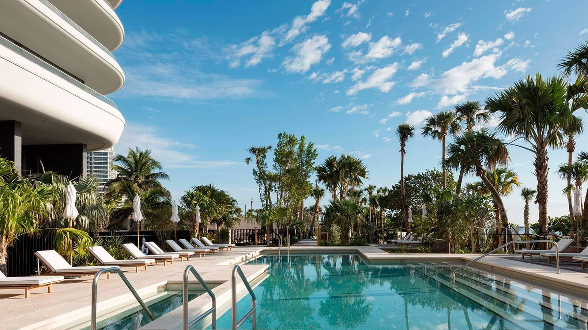Pool deck at Faena House in Miami Beach, luxury and ultra luxury condos with a curved exterior facade, palm trees, sun loungers, and a tranquil resort-style pool.