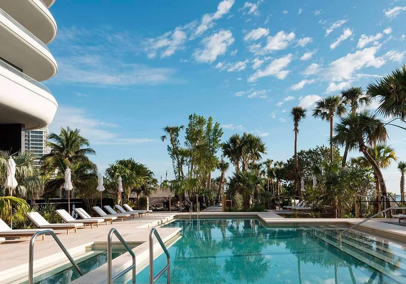 Pool deck at Faena House in Miami Beach, luxury and ultra luxury condos with a curved exterior facade, palm trees, sun loungers, and a tranquil resort-style pool.