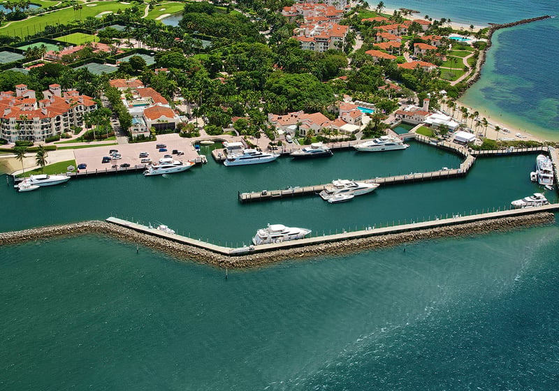 Fisher Island luxury and ultra luxury condos amenity with an aerial deep dockage marina, yachts, shoreline residences, and a sandy beach.