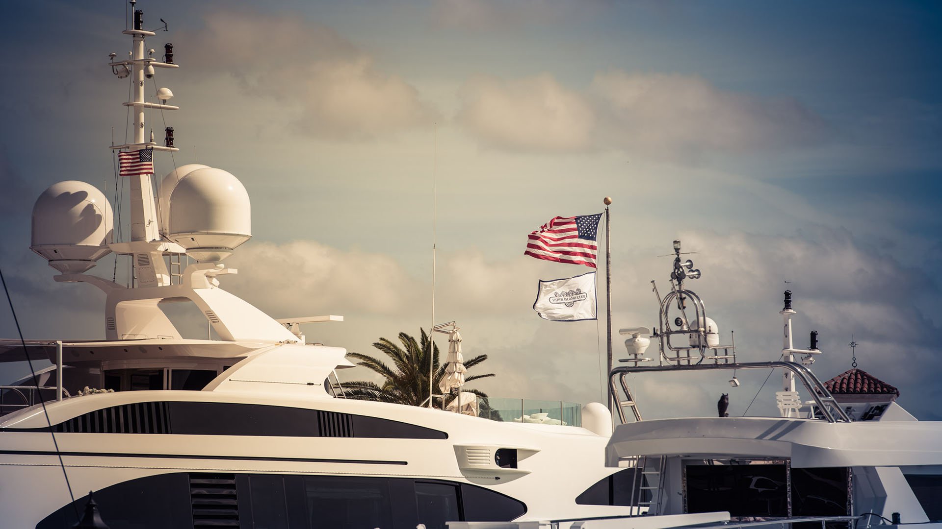 Fisher Island luxury and ultra luxury condos marina amenity with superyachts berthed at a deep dockage marina beneath club flags.