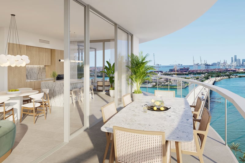 Wraparound balcony with marble dining table and bay skyline view at Five Park in Miami Beach, luxury and ultra luxury condos connected to an open kitchen and living area.