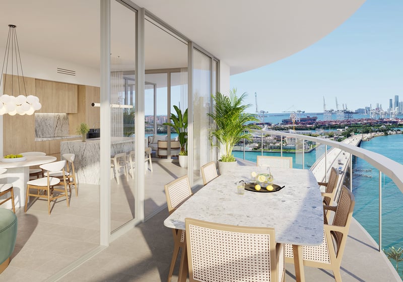 Wraparound balcony with marble dining table and bay skyline view at Five Park in Miami Beach, luxury and ultra luxury condos connected to an open kitchen and living area.