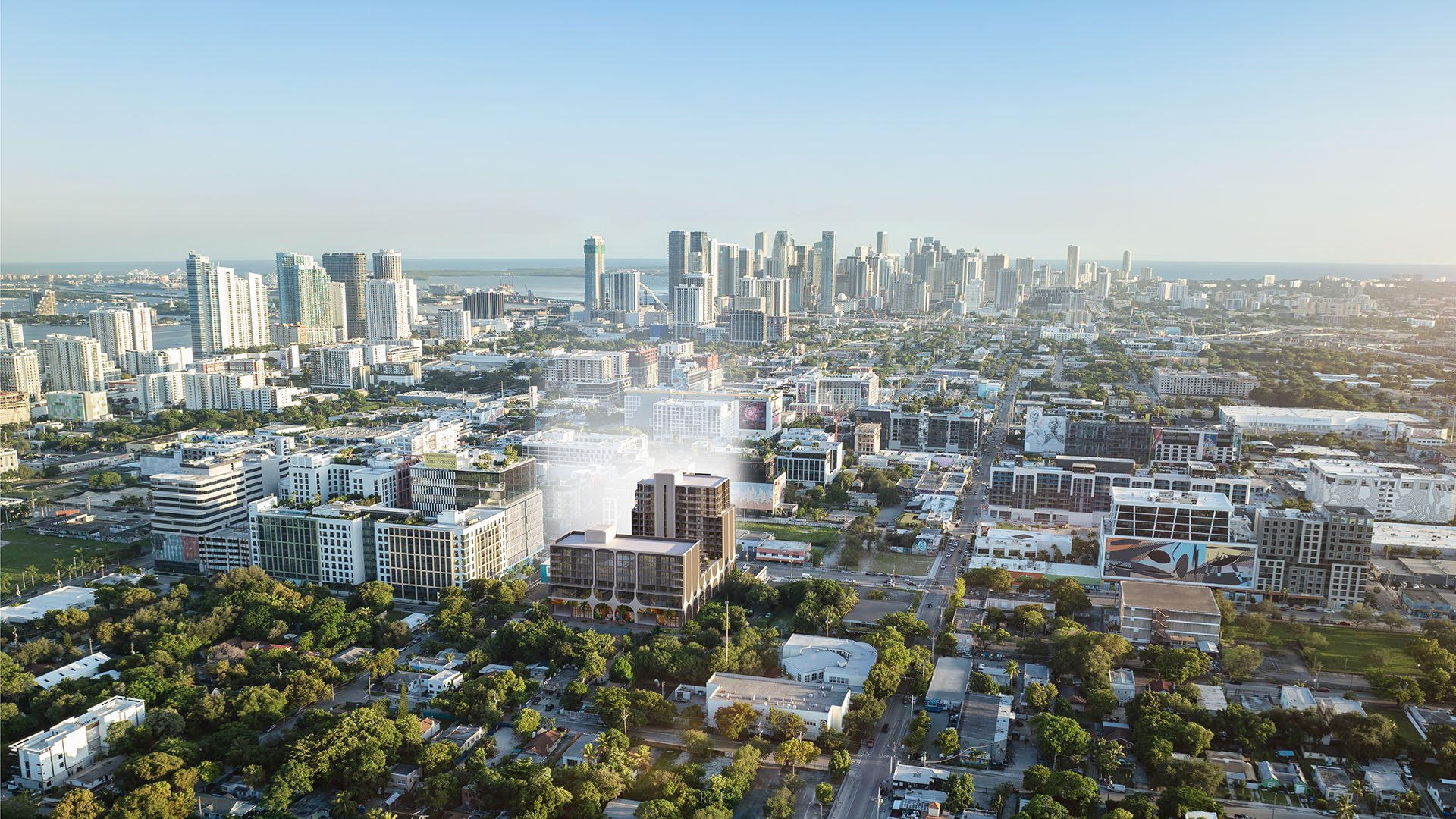 Aerial neighborhood view of Frida Kahlo Residences in Wynwood, showing luxury and ultra luxury condos with the project in the foreground and the downtown Miami skyline and bay beyond.