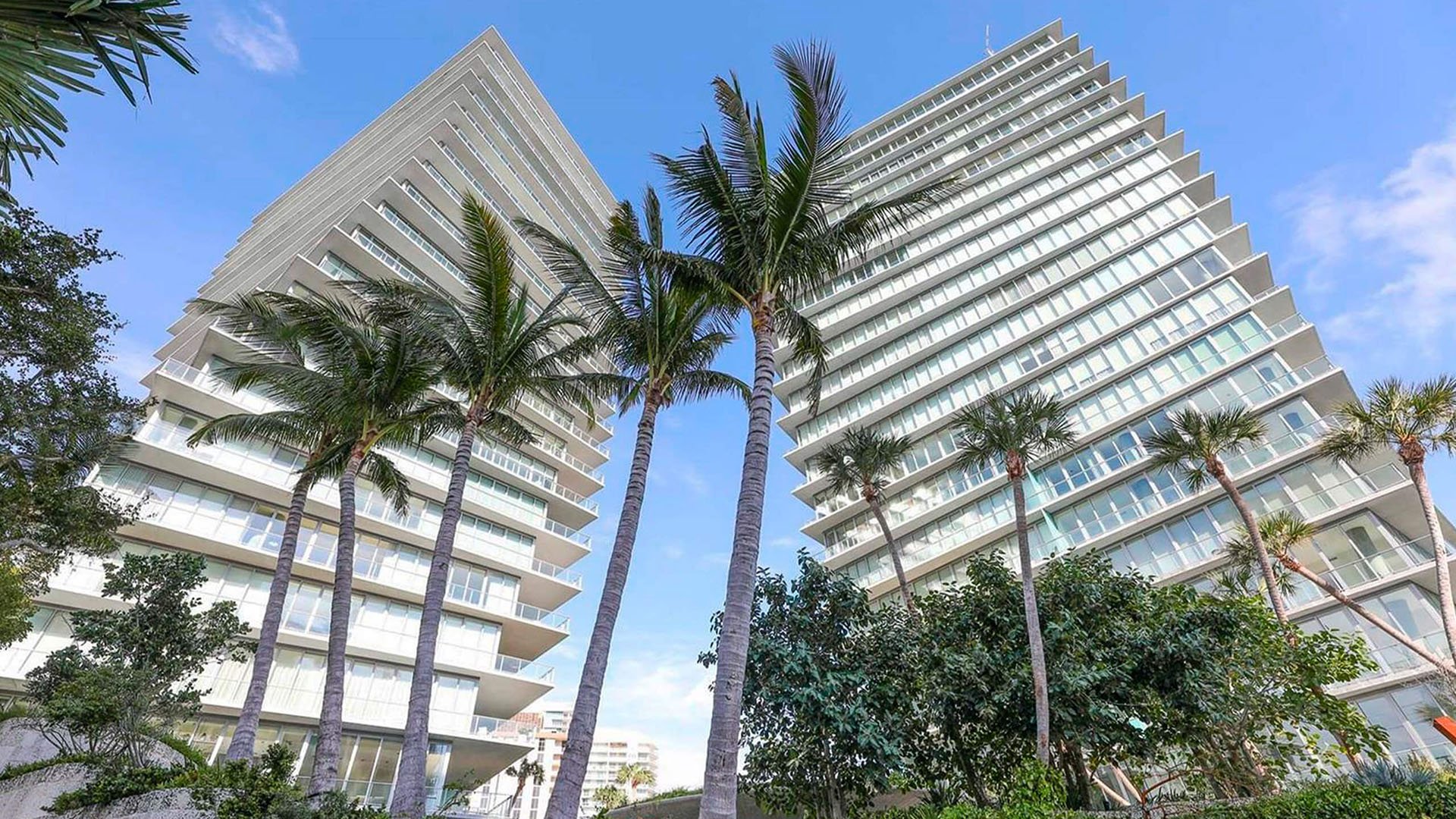 Grove at Grand Bay, Coconut Grove luxury and ultra luxury condos with an upward exterior view of both towers framed by tall palm trees and tropical landscaping.