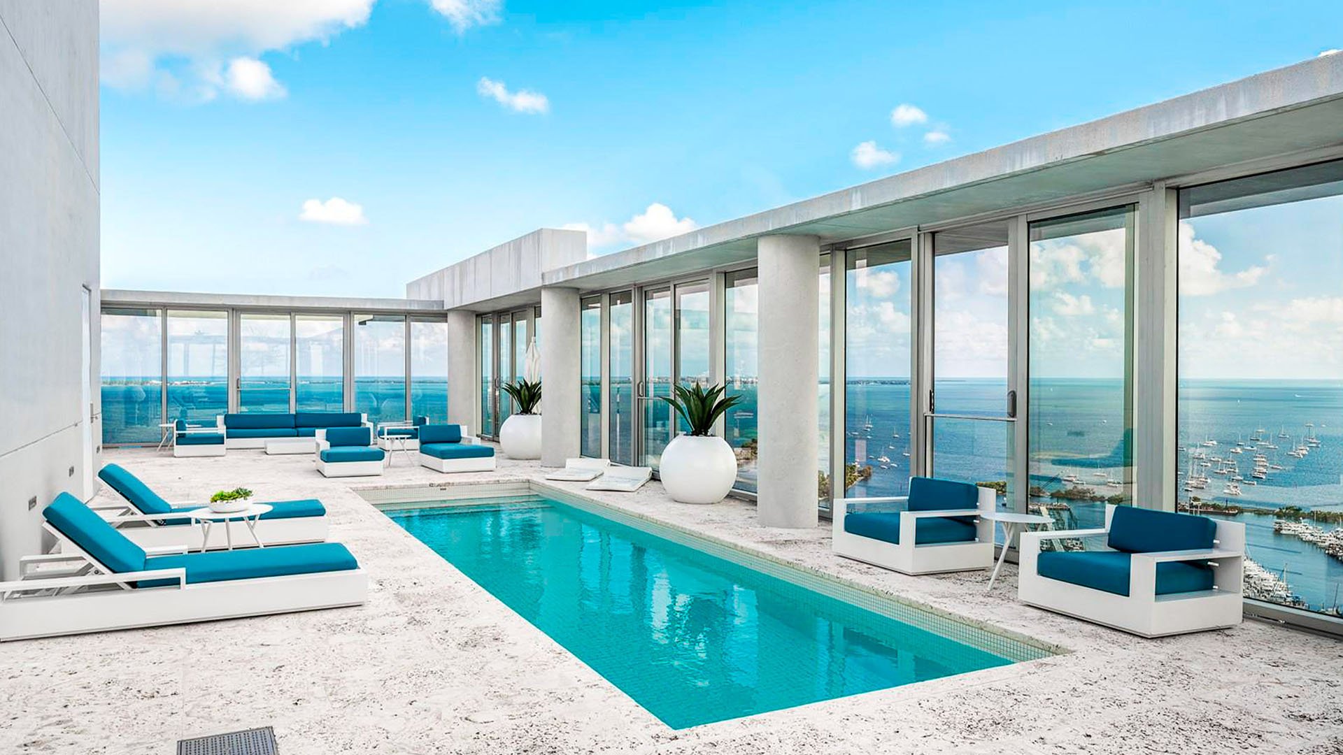 Grove at Grand Bay, Coconut Grove luxury and ultra luxury condos with a rooftop pool terrace, blue lounge seating, full-height glass, and panoramic marina views.