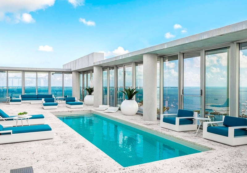 Grove at Grand Bay, Coconut Grove luxury and ultra luxury condos with a rooftop pool terrace, blue lounge seating, full-height glass, and panoramic marina views.