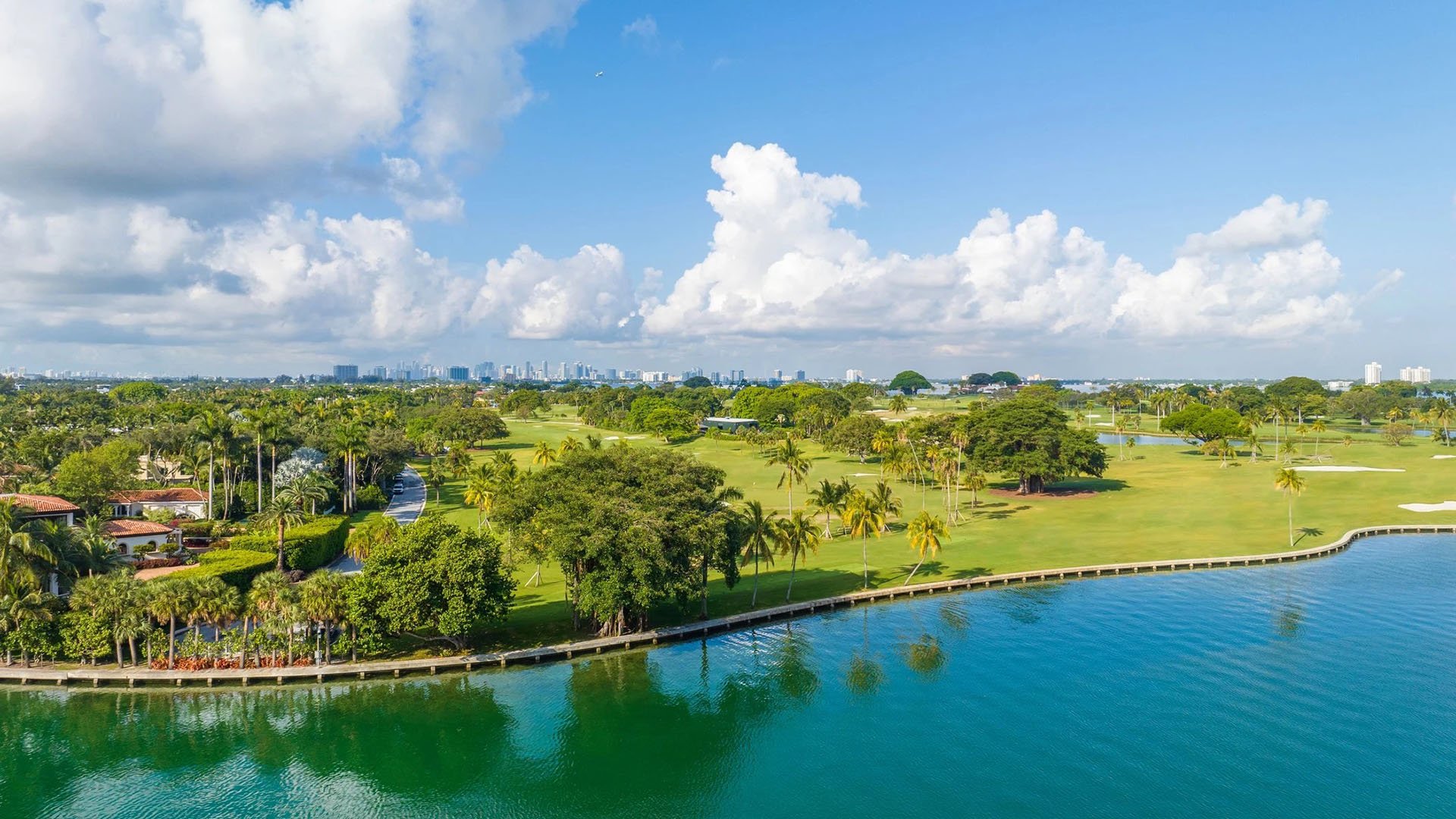 Indian Creek Residences and Yacht Club Bay Harbor Islands, Miami, Florida aerial showing waterfront golf course greens and tree-lined fairways with city skyline, highlighting the setting for luxury and ultra luxury preconstruction condos.