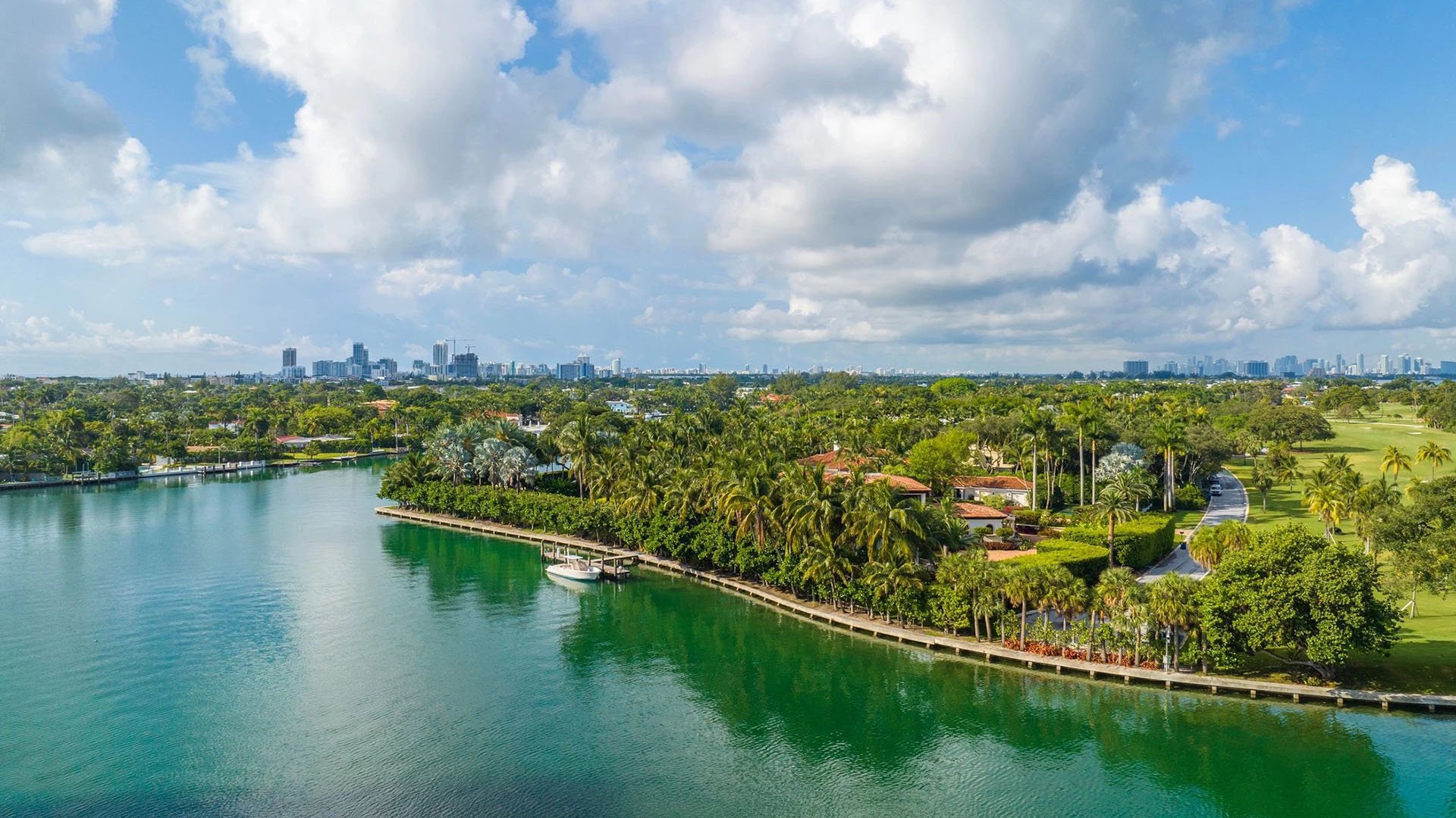 Indian Creek Residences and Yacht Club Bay Harbor Islands, Miami, Florida aerial of palm-lined canal waterfront, estate homes, private dock and boat with skyline views, reflecting luxury and ultra luxury preconstruction condos lifestyle.