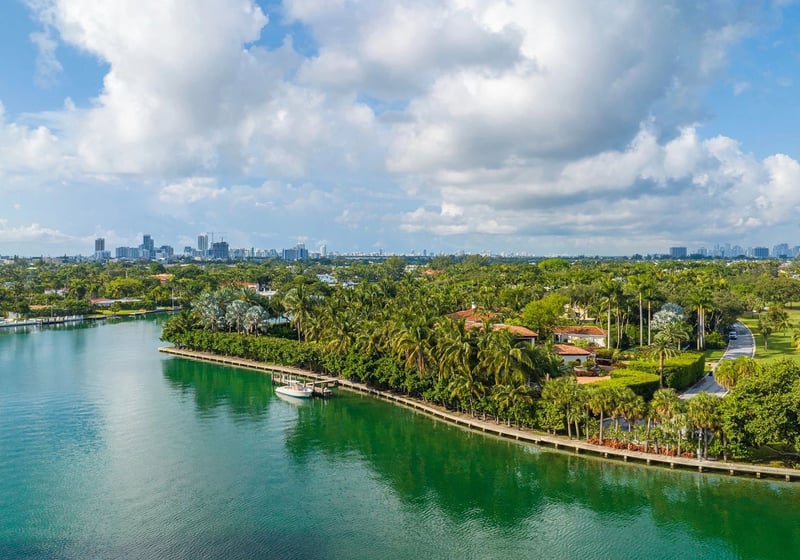 Indian Creek Residences and Yacht Club Bay Harbor Islands, Miami, Florida aerial of palm-lined canal waterfront, estate homes, private dock and boat with skyline views, reflecting luxury and ultra luxury preconstruction condos lifestyle.