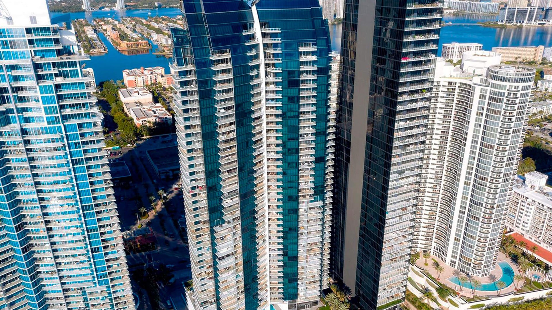 Aerial waterfront view of Jade Ocean in Sunny Isles Beach, featuring luxury and ultra luxury condos with the signature glass tower, neighboring high-rises, and the Intracoastal Waterway in the background.