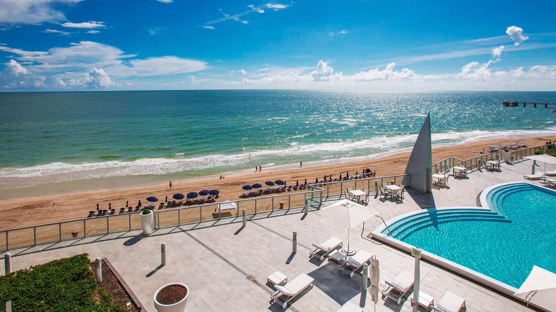 Elevated beachfront pool deck at Jade Ocean in Sunny Isles Beach, showing luxury and ultra luxury condos with a curved resort-style pool, expansive terrace seating, and sweeping Atlantic panorama.