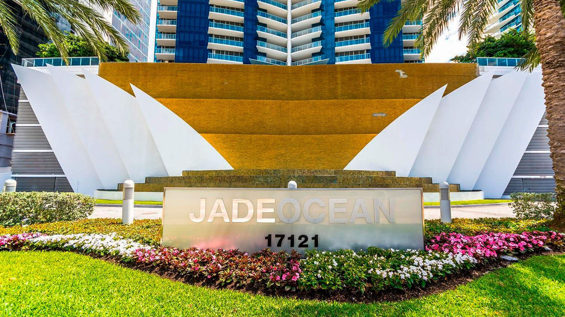 Entrance monument sign at Jade Ocean in Sunny Isles Beach for the luxury and ultra luxury condos, framed by a dramatic cascading waterfall wall, manicured landscaping, and the tower rising behind.