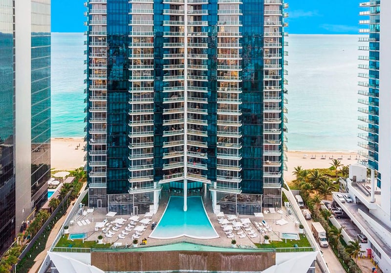 Oceanfront tower facade at Jade Ocean in Sunny Isles Beach, presenting luxury and ultra luxury condos above a dramatic podium pool deck with the beach and ocean directly behind the building.