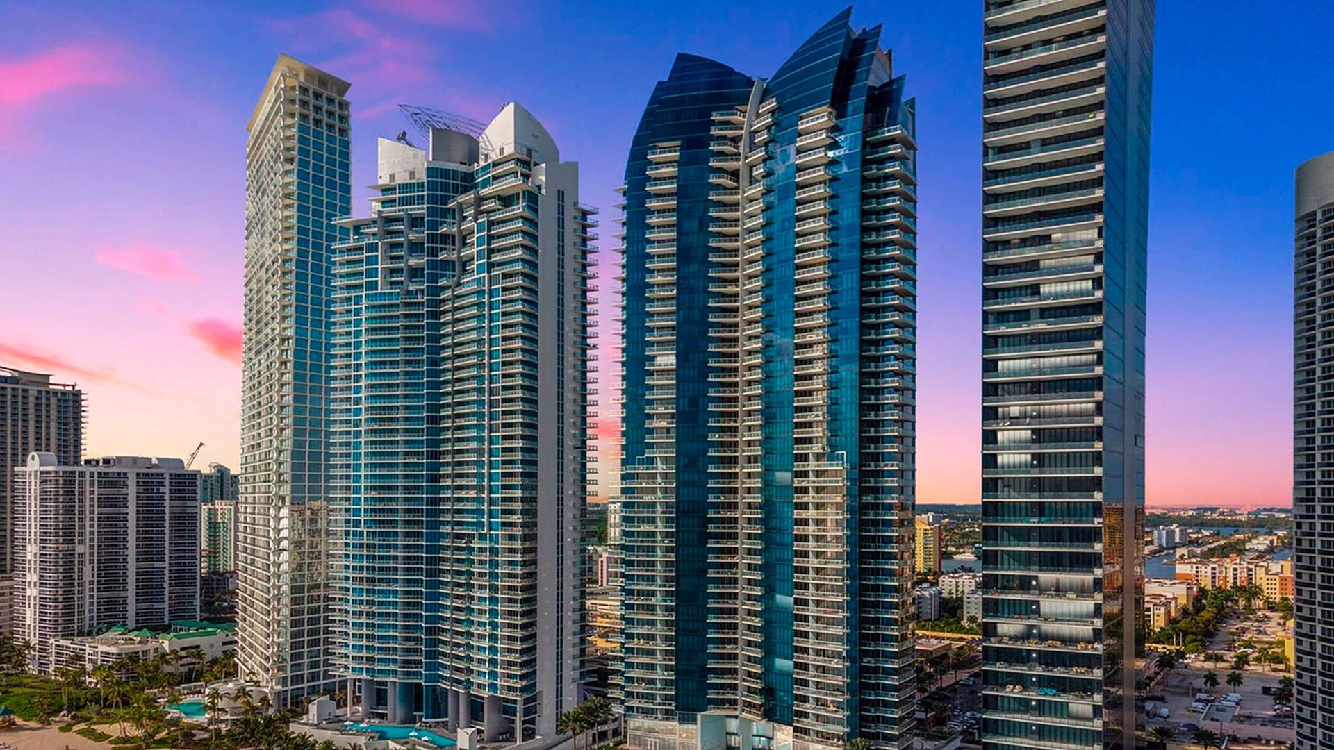 Twilight skyline view of Jade Ocean in Sunny Isles Beach, showcasing luxury and ultra luxury condos with the signature glass tower rising among neighboring high-rises at sunset.