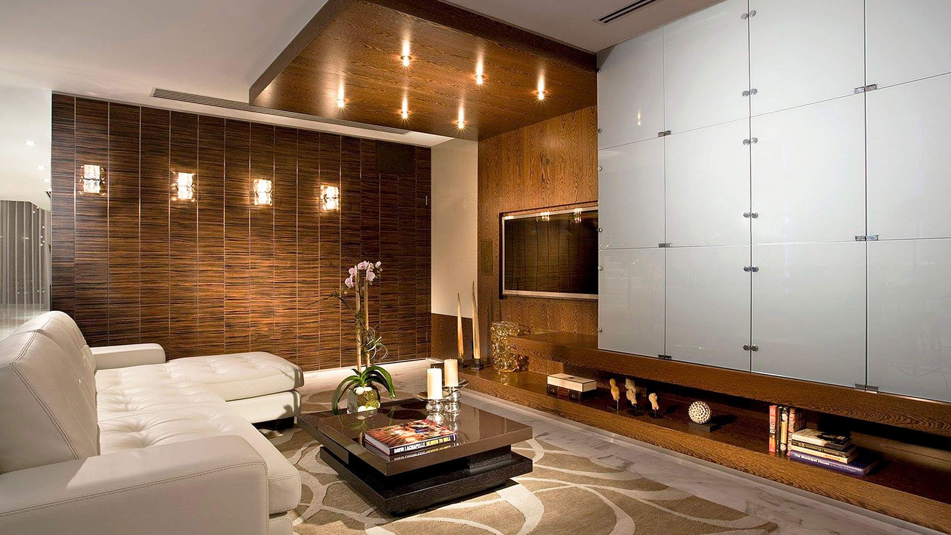 Wood-paneled media room inside one of the luxury and ultra luxury condos at Jade Ocean in Sunny Isles Beach, featuring built-in television cabinetry, warm lighting, white leather seating, and a modern lounge feel.