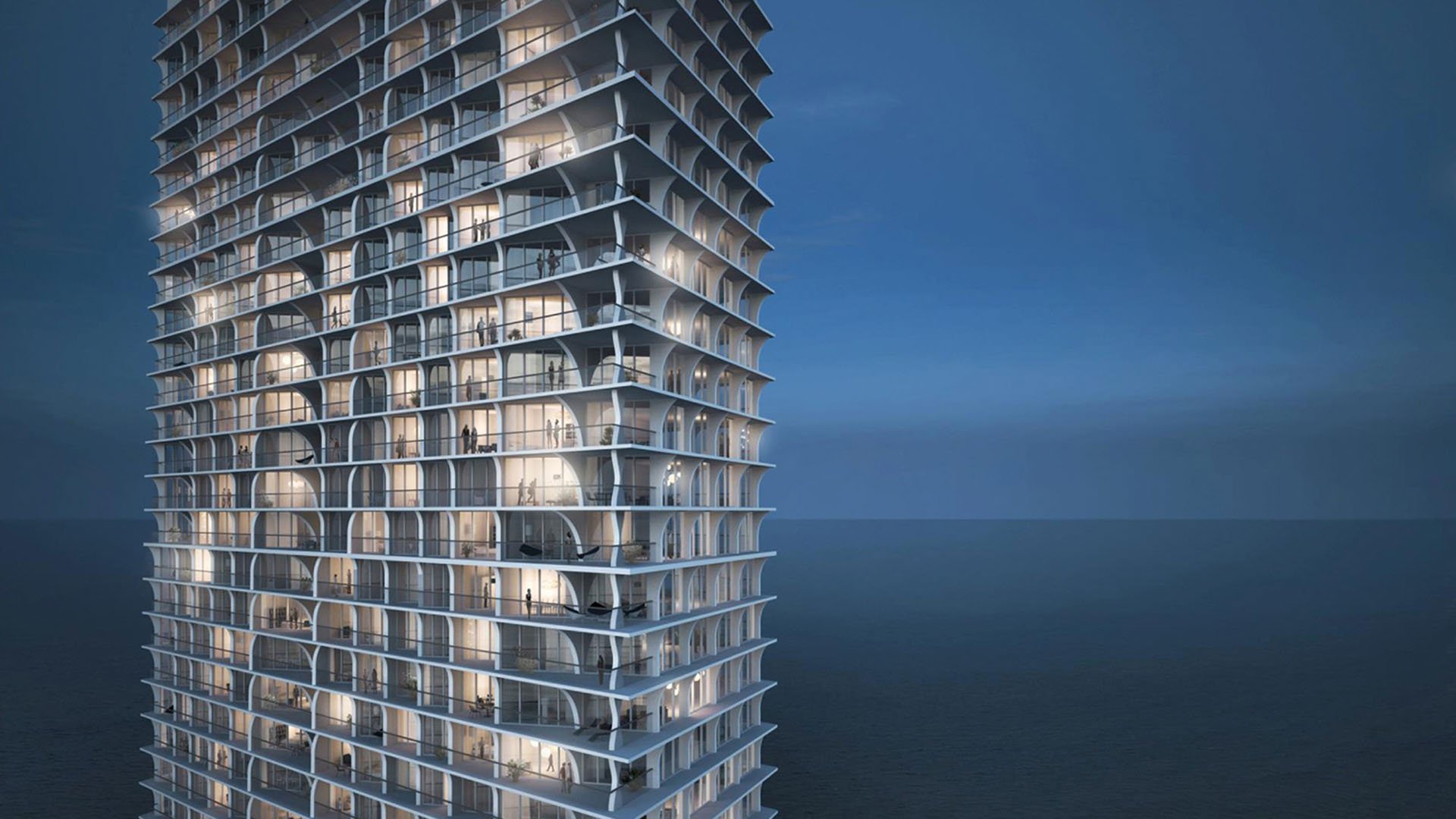 Jade Signature in Sunny Isles Beach luxury and ultra luxury condos closeup of the oceanfront tower facade at blue hour, showing curved balconies, floor to ceiling glass and the dark blue sea beyond.