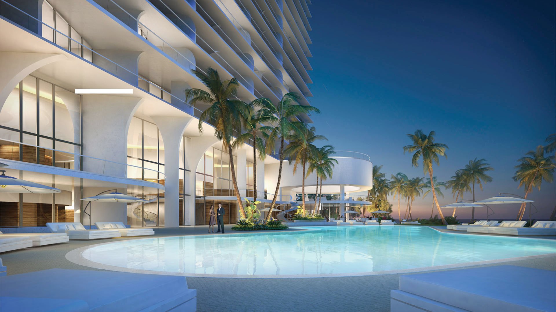 Jade Signature in Sunny Isles Beach luxury and ultra luxury condos with a twilight pool courtyard, circular pavilion, illuminated glass facade, palm trees and resort loungers facing the ocean.