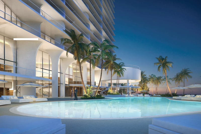 Jade Signature in Sunny Isles Beach luxury and ultra luxury condos with a twilight pool courtyard, circular pavilion, illuminated glass facade, palm trees and resort loungers facing the ocean.
