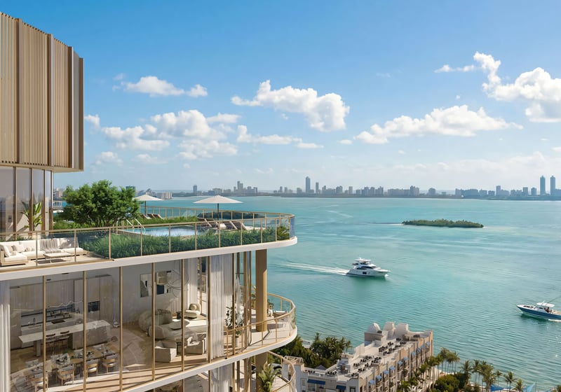 Kempinski Residences Miami in Miami Design District, luxury and ultra luxury condos, preconstruction exterior with a curved upper-level terrace, floor-to-ceiling glass, a landscaped lounge deck, and broad waterfront skyline views with boats.