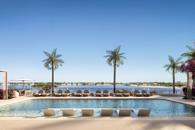 Daytime waterfront pool terrace with submerged loungers, palm trees and pergolas at Maison D'Or in West Palm Beach, showcasing luxury and ultra luxury preconstruction condos beside the water.