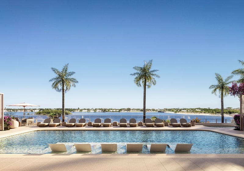 Daytime waterfront pool terrace with submerged loungers, palm trees and pergolas at Maison D'Or in West Palm Beach, showcasing luxury and ultra luxury preconstruction condos beside the water.