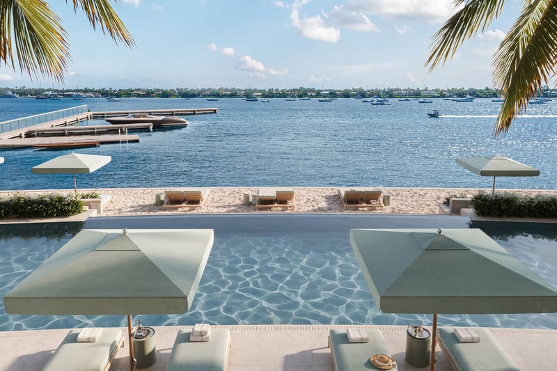 Poolside umbrellas and sandy loungers overlook a dock and open waterfront at Mandarin Oriental Residences, West Palm Beach, ultra luxury condos in West Palm Beach with a luxury resort-style water view.