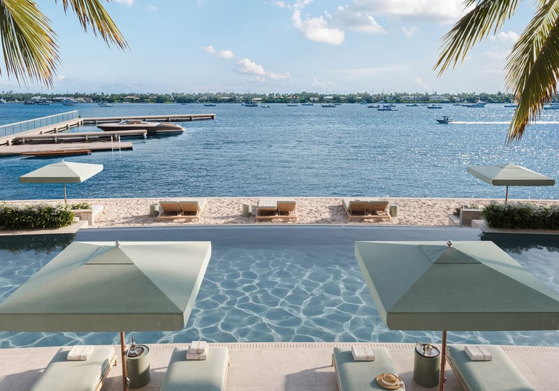Poolside umbrellas and sandy loungers overlook a dock and open waterfront at Mandarin Oriental Residences, West Palm Beach, ultra luxury condos in West Palm Beach with a luxury resort-style water view.