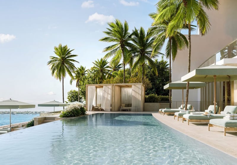 Long waterfront pool lined with loungers, palms, and a curtained cabana at Mandarin Oriental Residences, West Palm Beach, ultra luxury condos in West Palm Beach with a luxury outdoor amenity setting.