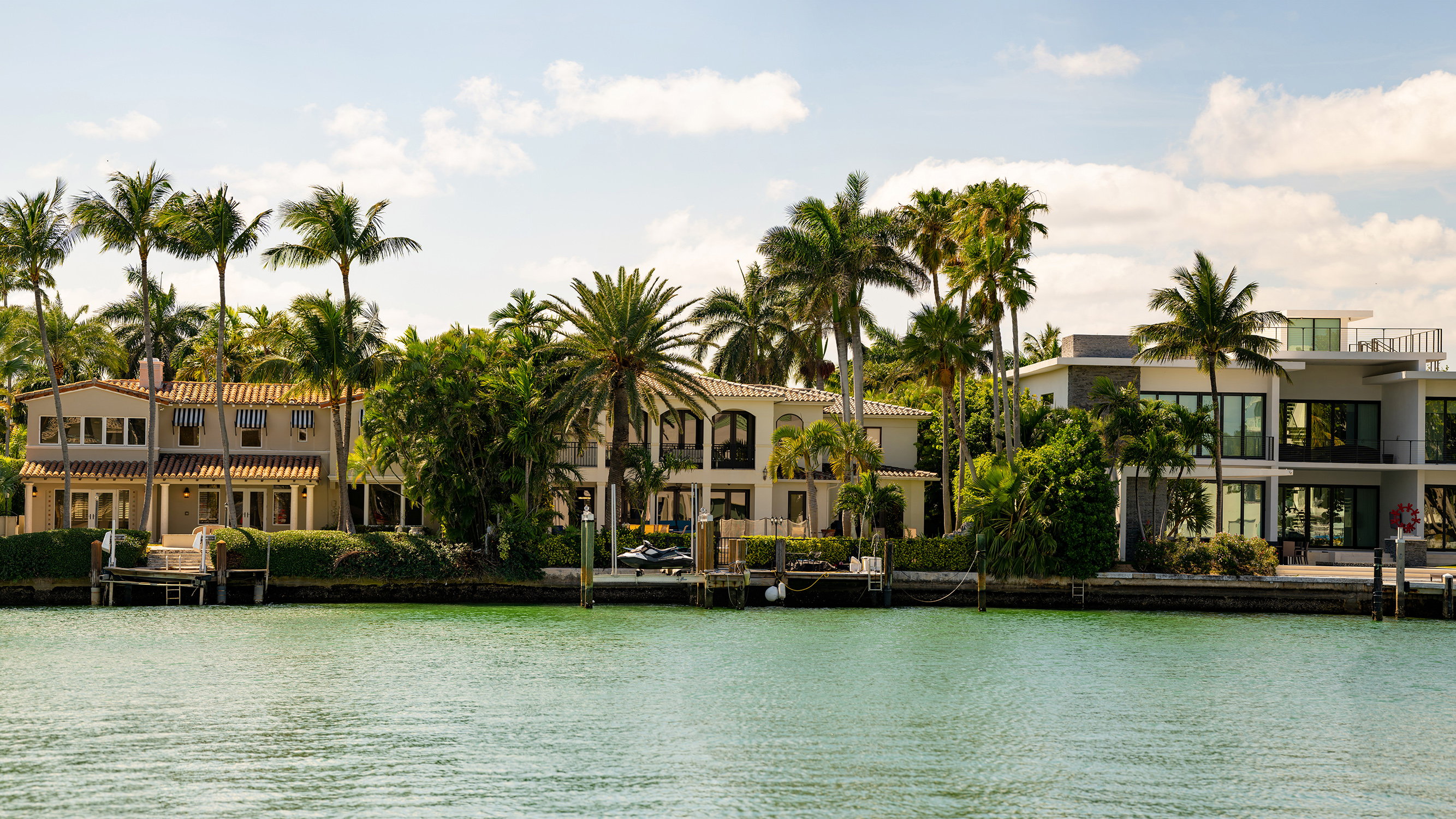 Miami Beach coastal homes with palms along canals, tropical waterfront living near luxury and ultra luxury condos; strong resale. Featuring palm trees.