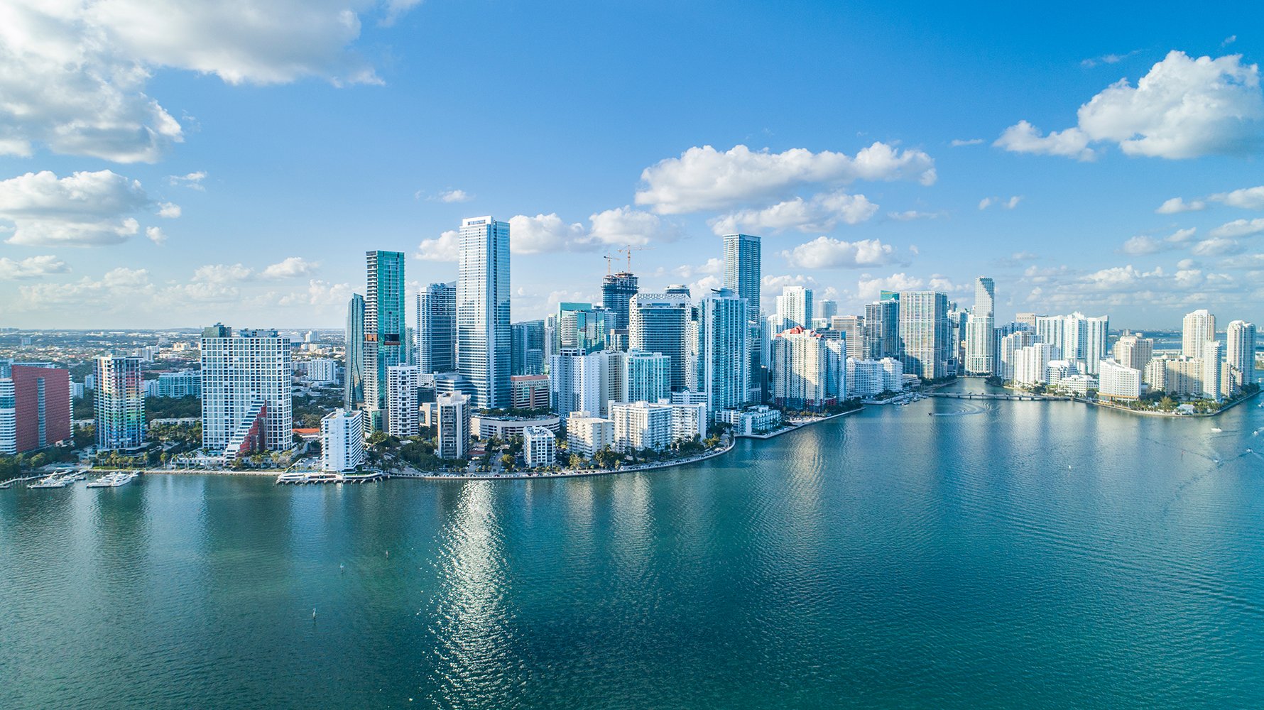 Miami skyline aerial over Biscayne Bay with bridges and islands, dynamic urban coast featuring luxury and ultra luxury condos; preconstruction and resale opportunities. Featuring view.