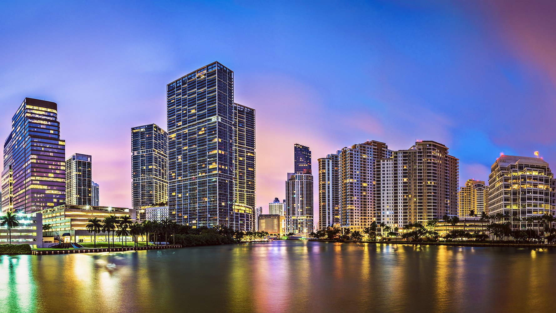 Miami sunset cityscape with illuminated towers; luxury and ultra luxury condos, preconstruction living in Miami’s urban core.