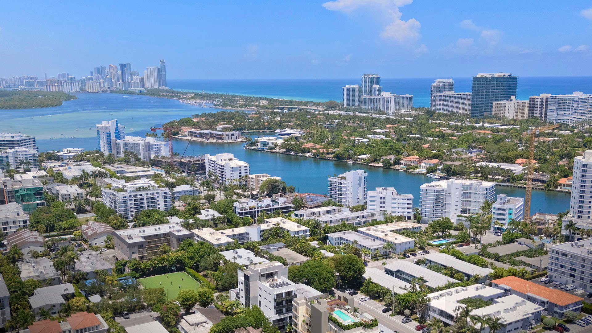 Mila Bay Harbor Islands preconstruction luxury and ultra luxury condos in Bay Harbor Islands with an aerial view over the waterfront neighborhood, bay, and ocean beyond nearby residences and waterways.