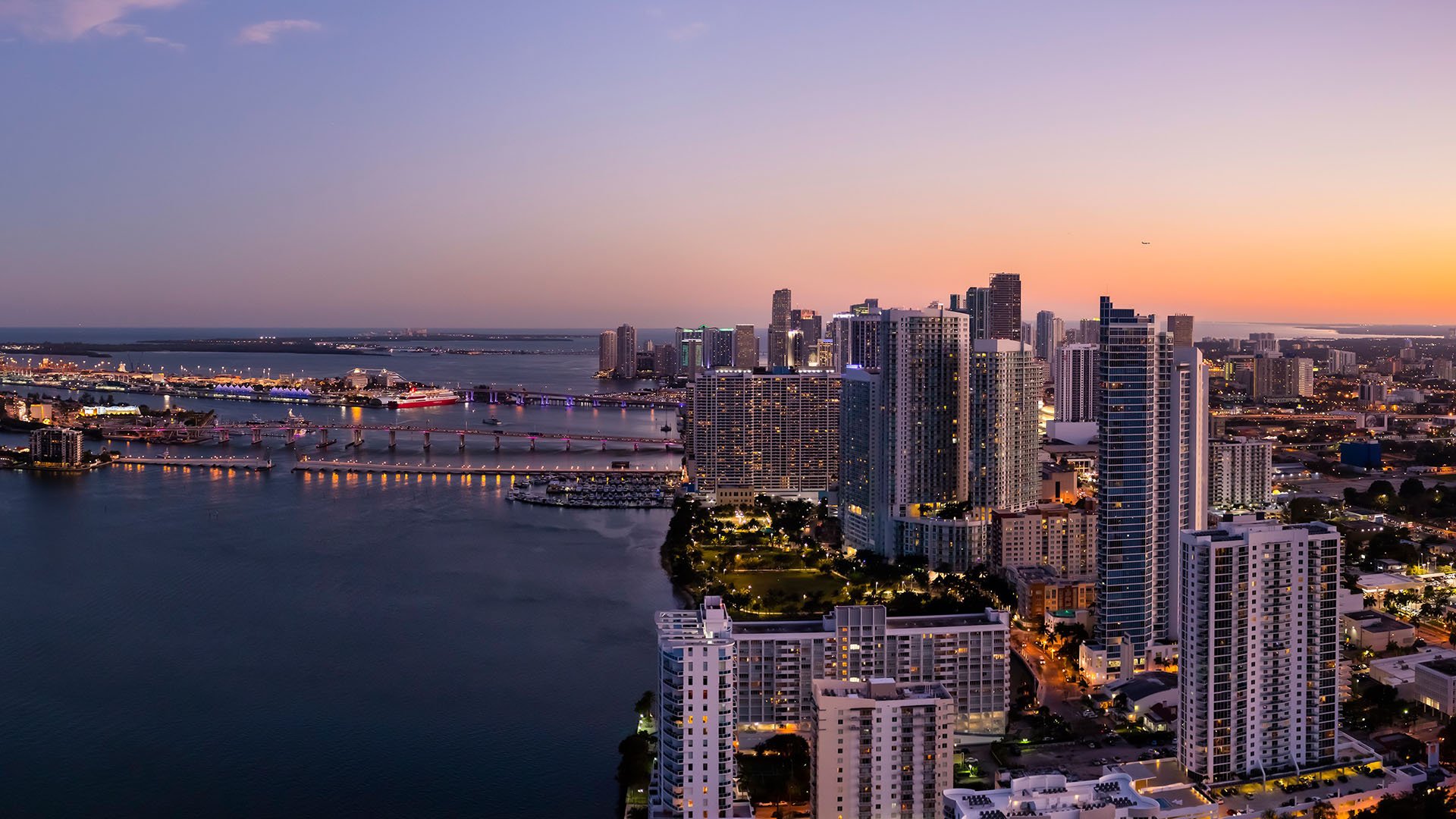 Missoni Baia Edgewater Miami south aerial at sunset toward Downtown skyline and Biscayne Bay bridges, showcasing luxury and ultra luxury preconstruction condos location.