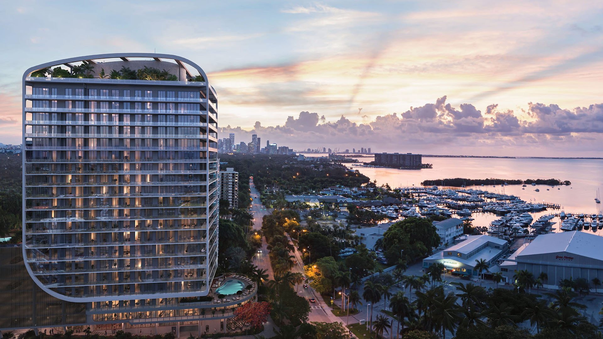 Aerial sunset view of the curved waterfront tower and marina at Mr C Residences Bayshore Tower in Coconut Grove, showcasing luxury, ultra luxury condos with a dramatic bayside skyline presence.