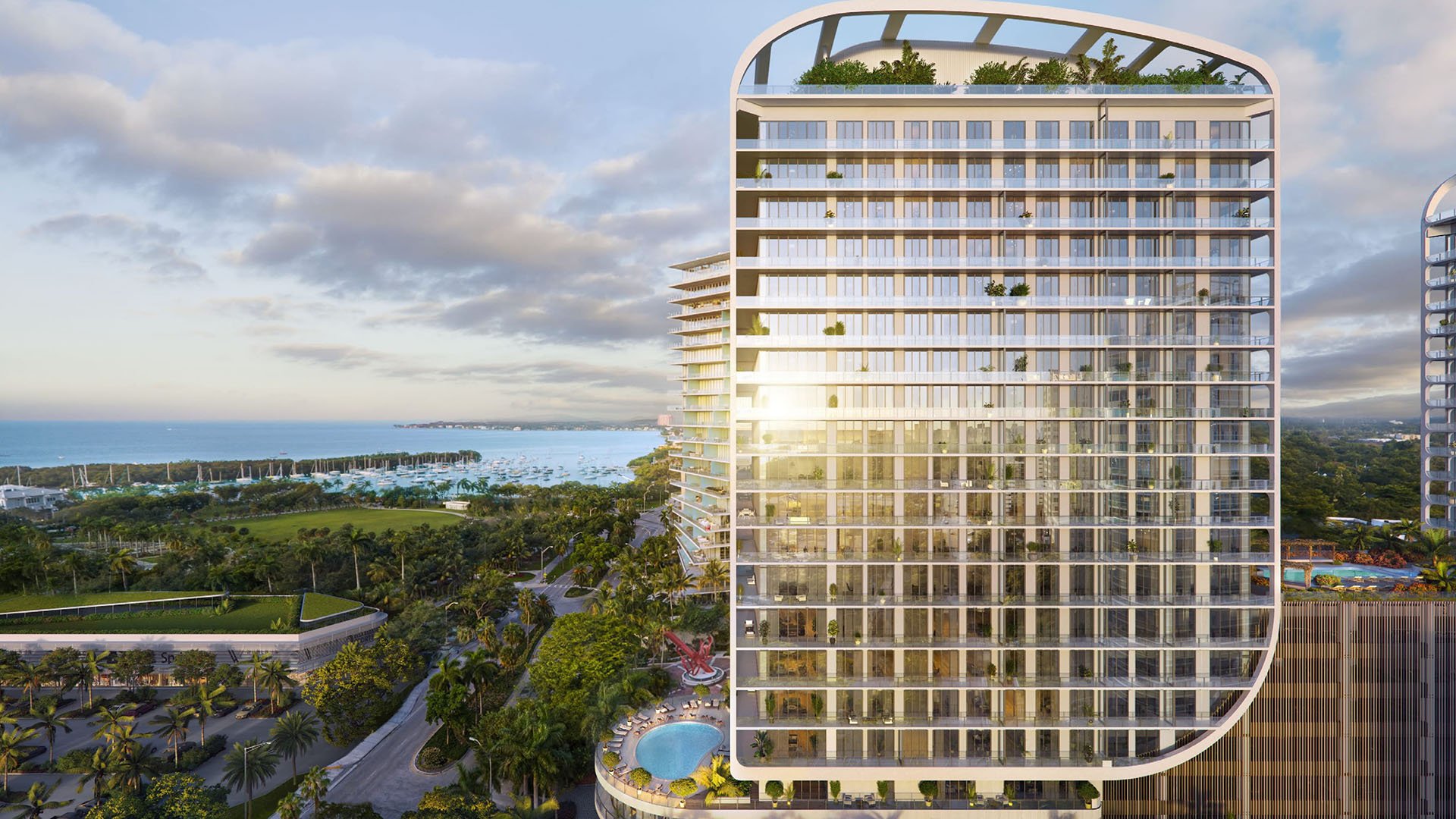 Bayfront tower elevation with marina views and a glowing glass facade at Mr C Residences Bayshore Tower in Coconut Grove, presenting luxury, ultra luxury condos with elegant curved architecture.