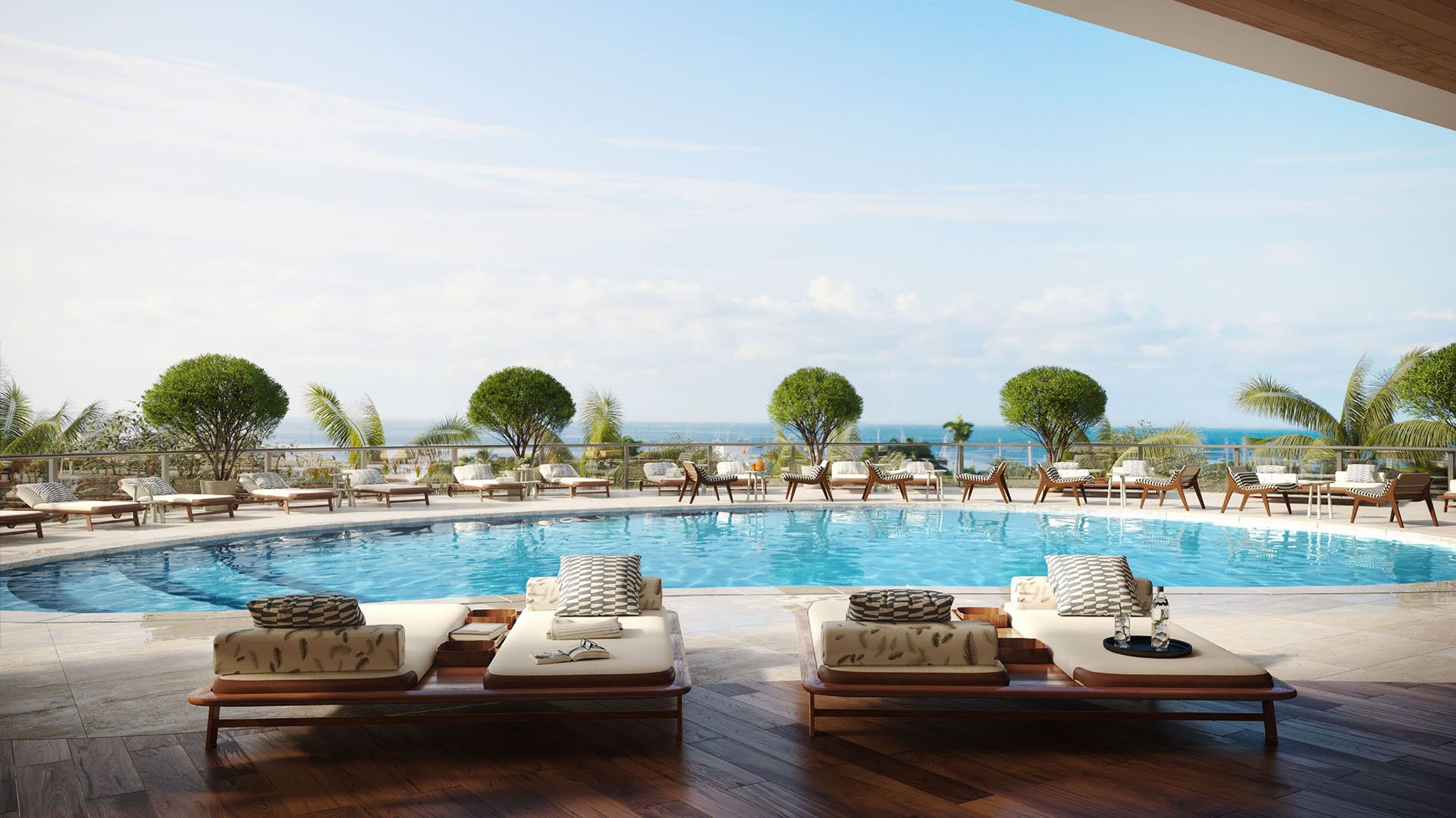 Resort pool deck with loungers, clipped greenery, and open water views at Mr C Residences Bayshore Tower in Coconut Grove, highlighting luxury, ultra luxury condos with a serene waterfront leisure setting.
