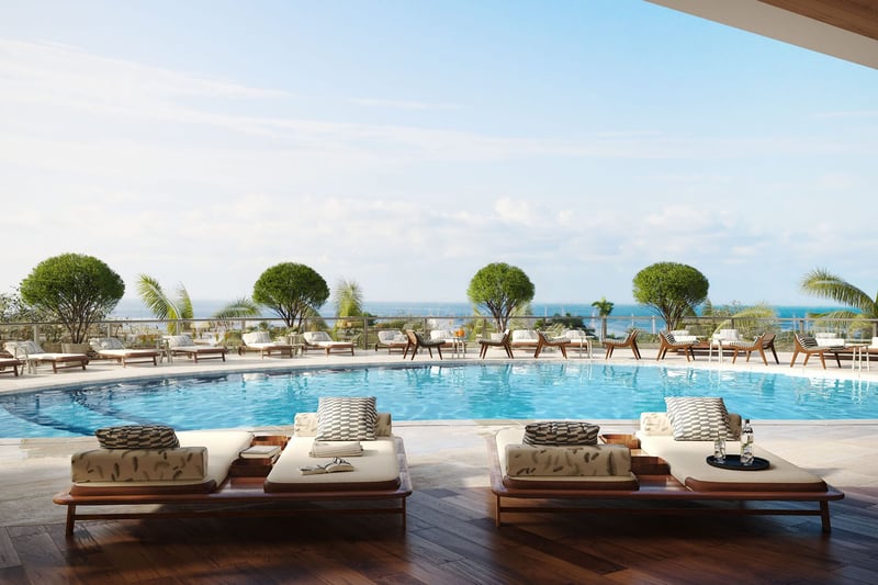Resort pool deck with loungers, clipped greenery, and open water views at Mr C Residences Bayshore Tower in Coconut Grove, highlighting luxury, ultra luxury condos with a serene waterfront leisure setting.